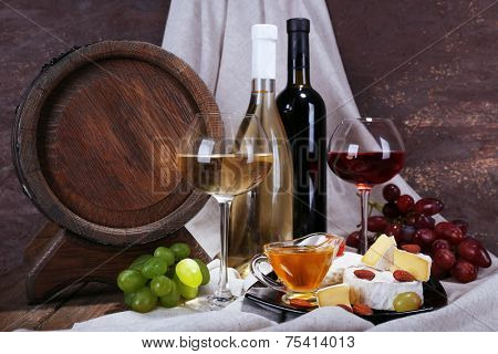 Supper consisting of Camembert and Brie cheese, honey, wine and grapes on napkin and wine barrel on curtain background
