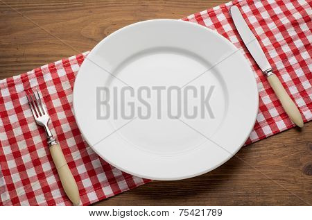 Empty plate with fork and knife on tablecloth over wooden