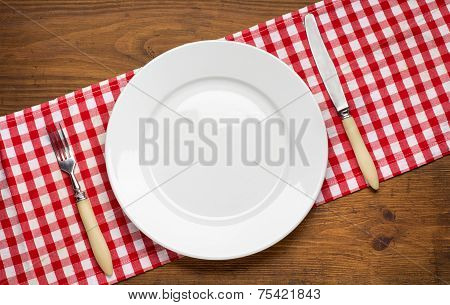 Empty plate with fork and knife on wooden table.