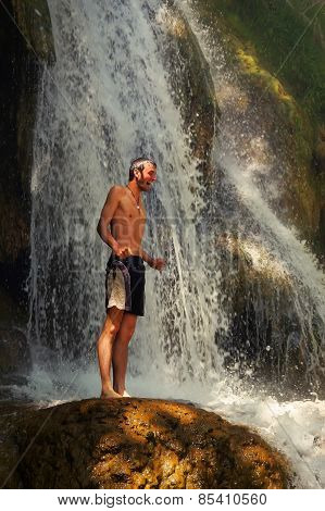 young man shrieking with joy standing on rock beside a beautiful waterfall