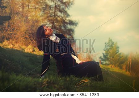 young woman with dark hair and a historical dress posing on a meadow in open lanscape