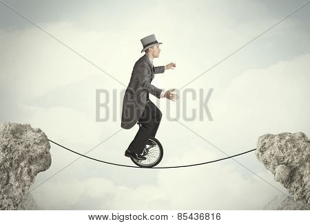 Brave business man riding an mono cycle between cliffs concept