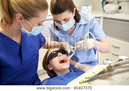 people, medicine, stomatology and health care concept - female dentists with mirror and suction treating patient girl teeth at dental clinic office