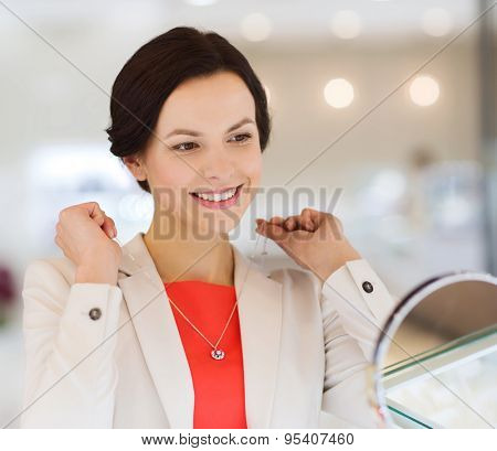 sale, consumerism, shopping and people concept - happy woman choosing and trying on pendant at jewelry store