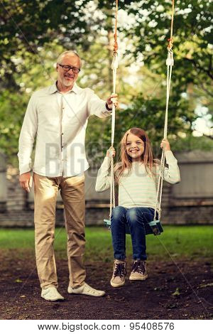 family, happiness, generation, home and people concept - happy grandfather and  granddaughter swinging on teeterboard outdoors