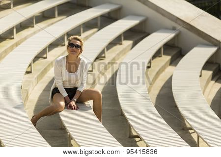 Young beautiful blondie woman sitting on benches in the Royal Baths Park in Warsaw, Poland.