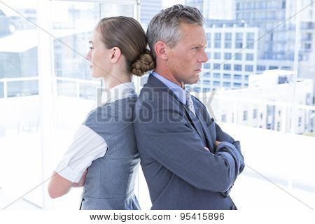 Two angry business colleagues standing back to back in the office