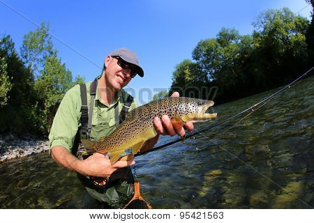 Closeup of fly-fisherman holding brown truit in river