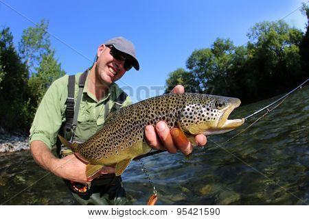 Closeup of fly-fisherman holding brown truit in river