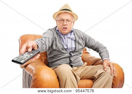 Angry senior man pressing buttons on a remote control seated in an armchair isolated on white background