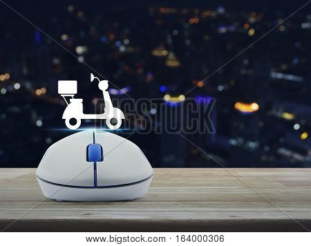 Wireless computer mouse with motor bike icon on wooden table over blur light city tower Business internet delivery service concept