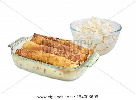 Pancakes filled with cottage cheese in the rectangular glass roasting pan and glass bowl with fresh cottage cheese on a light background