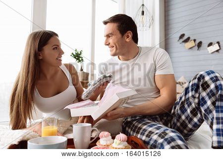 Keeping warmth. Positive nice attractive woman holding looking at her boyfriend and smiling while holding a knitted cap