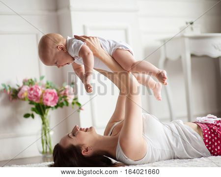 Young mother playing with her baby. She throws up him and they are gaily laughing .