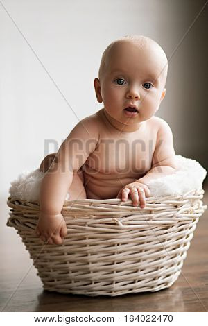 Little baby sits in a wicker basket. He looks very surprised.