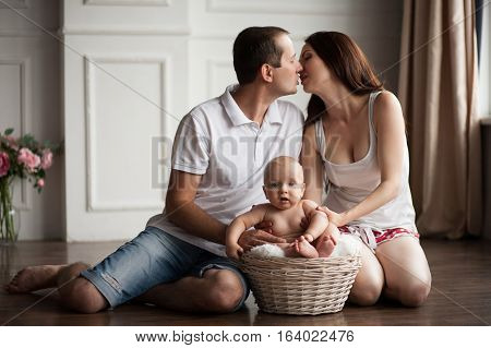 Happy young parents close to small baby in wicker basket. Parents kissing and hugging their child.
