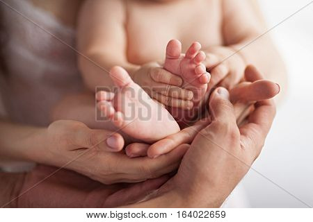 Baby in mother's and father's hands. Both parents support child's feet with his hands. Close up.