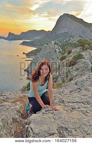 The girl sits on a high hill by the sea at sunset. Sudak. Crimea