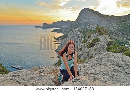 The girl sits on a high hill by the sea at sunset. Sudak. Crimea