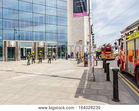 Firefighters outside a building.
Dublin, Ireland - April 21, 2016: Two fire engines and a group of firefighters from Dublin Fire Brigade outside a building. 
Firefighters talking. People passing by.