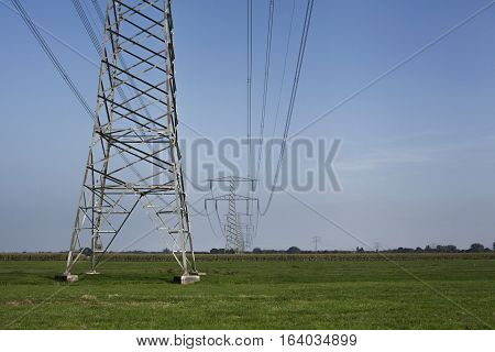 High voltage electrical transmission towers electricity pylons and power lines on green field
