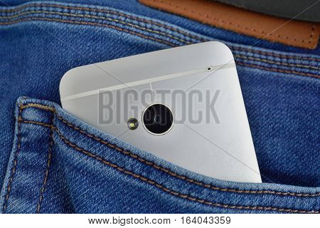 Silver aluminum smartphone placed at the male stitched blue jean's backpocket