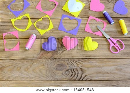 Valentine's day hearts crafts. Colorful hearts gifts made of felt, felt scraps, scissors, thread on wooden table. Valentine's day handmade gifts concept. Needlework background. Top view