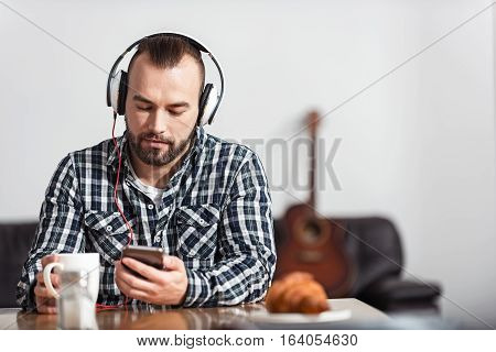 Checking out new tracks. Attractive stylish young man enjoying his lunch while listening to some music and wearing headphones