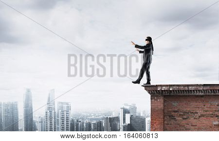 Businessman with blindfolder on eyes walking on building top