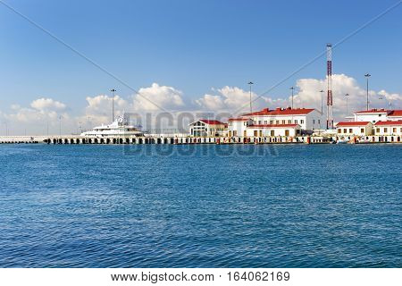 Luxury yacht moored at pier in Sochi seaport. In background is concrete promenade and Black sea. Marine station complex Port. Krasnodarskiy kray Russia