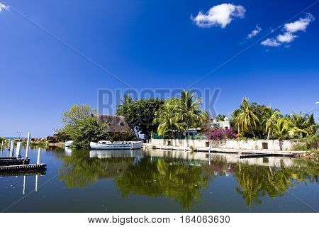 Seascape with bright blue skies, old houses, dock, boat and palm trees.