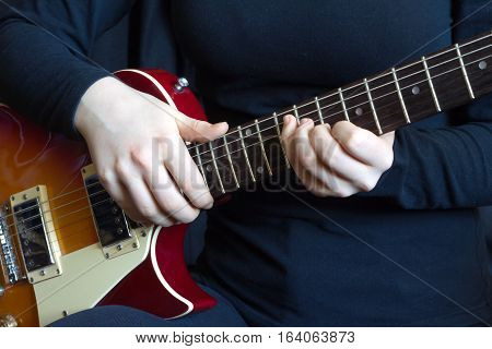 Musician in black on red six strings electric guitar playing. Hands of the musician closeup