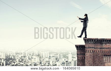 Businessman with blindfolder on eyes walking on building top