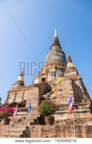 Buddha statue at the bottom of a large ancient pagoda on blue sky background at Wat Yai Chai Mongkon temple in Phra Nakhon Si Ayutthaya Historical Park Ayutthaya Province Thailand
