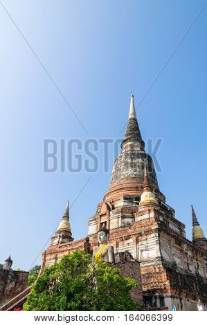 Buddha statue at the bottom of a large ancient pagoda on blue sky background at Wat Yai Chai Mongkon temple in Phra Nakhon Si Ayutthaya Historical Park Ayutthaya Province Thailand
