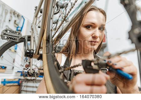 Painstaking job. Charming positive skilled mechanic standing in the garage and working while fixing the chain of the bicycle