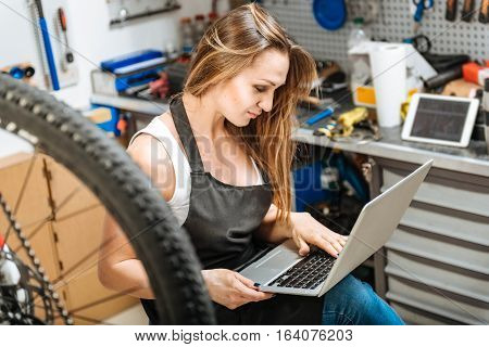 Useful devices for my work. Appealing beefy young technician sitting in the garage and expressing happiness while using the laptop and working