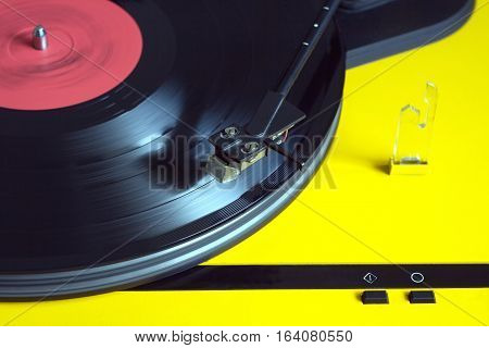 Turntable in yellow case playing a vinyl record with red label. Horizontal photo top view closeup
