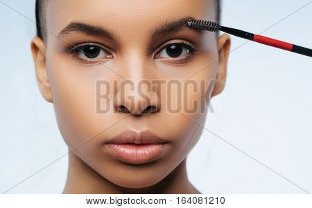 Perfect shape. Beautiful nice brunette woman looking at you and using special brush while making the shape of her eyebrows perfect