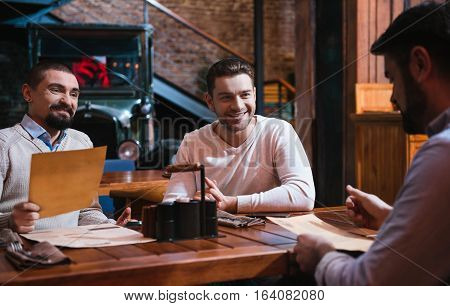 Deciding what to order. Cheerful pleasant nice men sitting together at the table and discussing menus while deciding what to choose