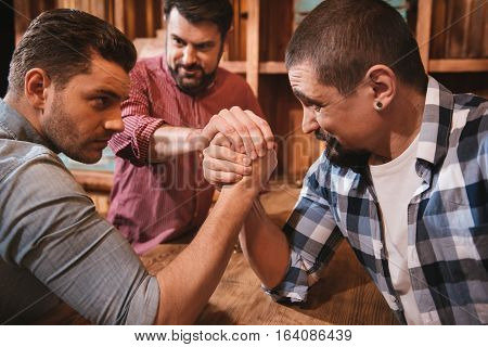 Fixed gaze. Handsome serious concentrated men looking at each other and gathering their strength while preparing to start an armwrestling match