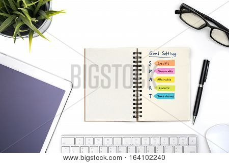 Smart goal setting with notebook eye glasses pen mouse keyboard tablet and plant on white desk Success concept
