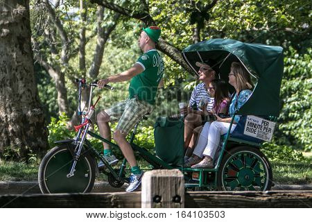 New York, June 25, 2016: A man operating a rickshaw is giving a tour to New York City visitors in Central Park.
