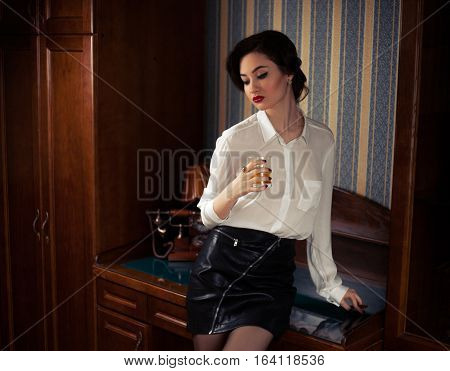 Girl near table in atmosphere of retro. She sat down at table with glass of whiskey in hand.