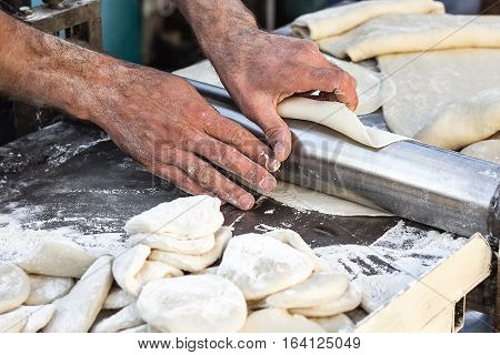 Chef making dough pastry sheeter at bakery Baker forming shaping dough rolled pastry metal work table closeup hands process of preparing bread khinkali dough roller machine thin pasta sheet Top view