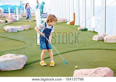 Little kid boy playing mini golf on a cruise liner. Child having fun with active leisure on vacations.