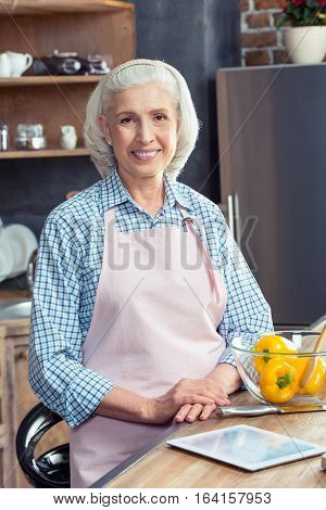Senior woman in apron smiling at camera in kitchen