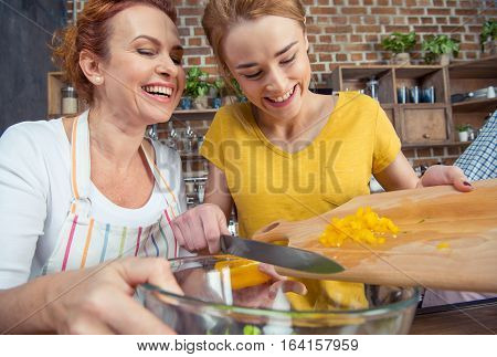 Happy mother and teenage daughter cooking vegetable salad together