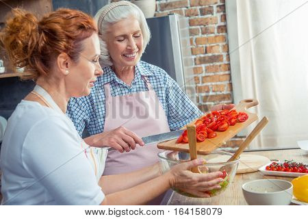 Smiling women in aprons cooking together in kitchen