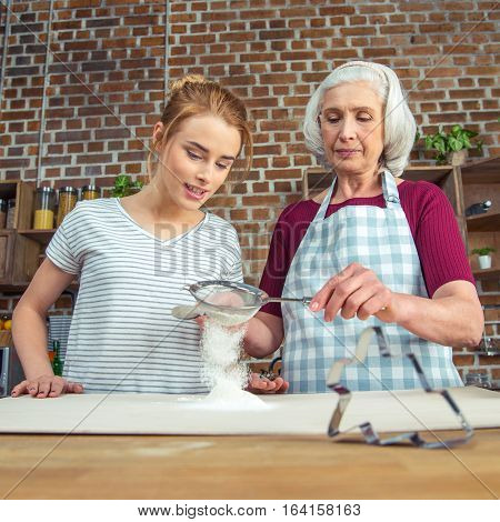 Grandmother and granddaughter sifting flour for cookies in kitchen